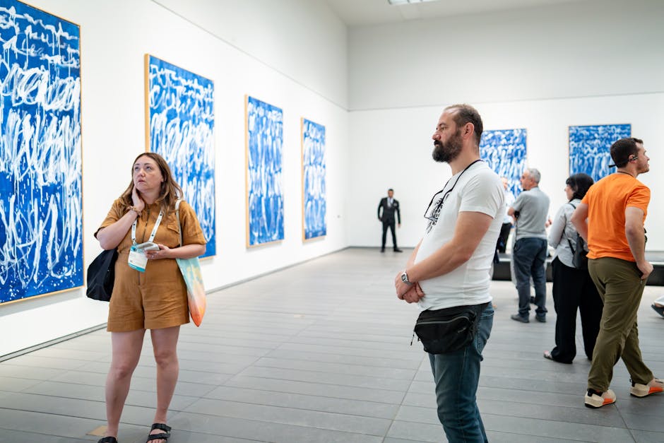 Visitors in an art gallery engaging with blue abstract artworks. Captured indoors with contemporary art, diverse visitors enhancing the scene.